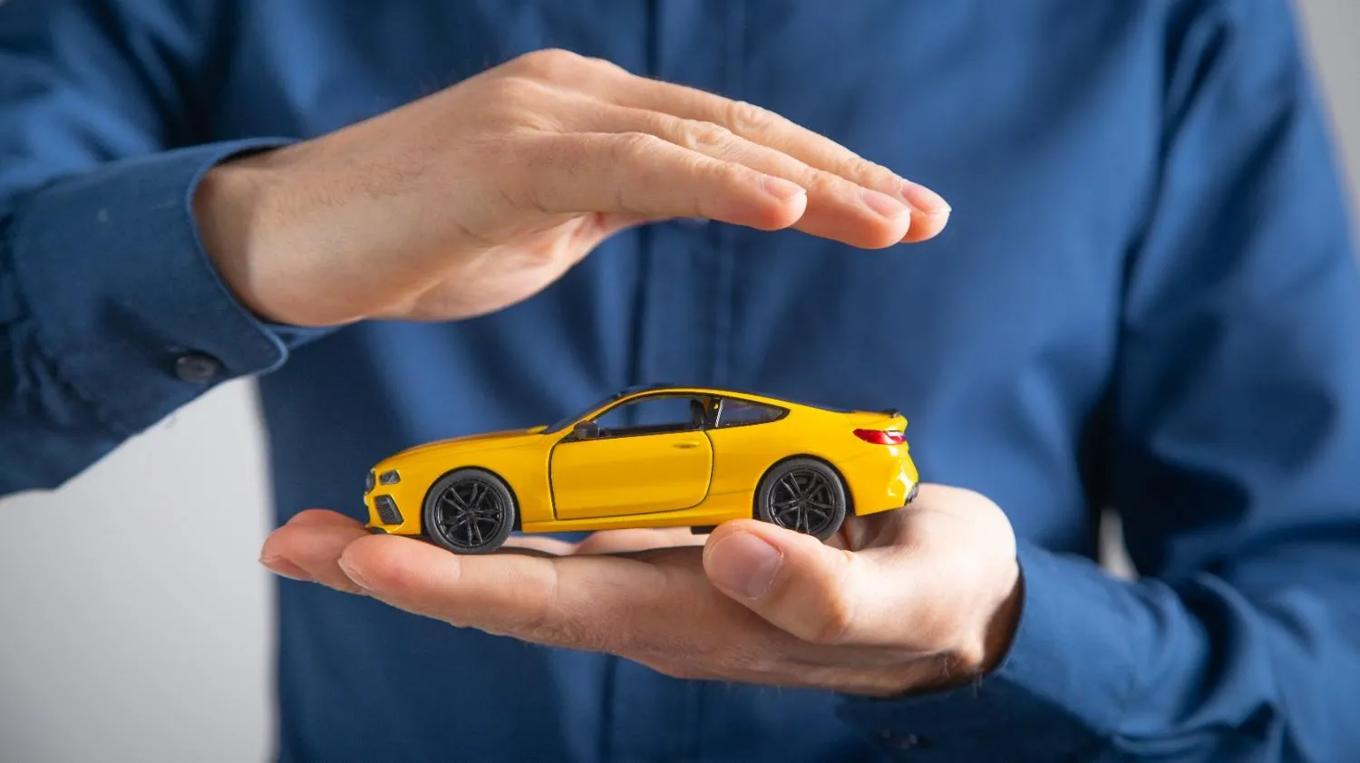 A person holding a small yellow car in cupped hands